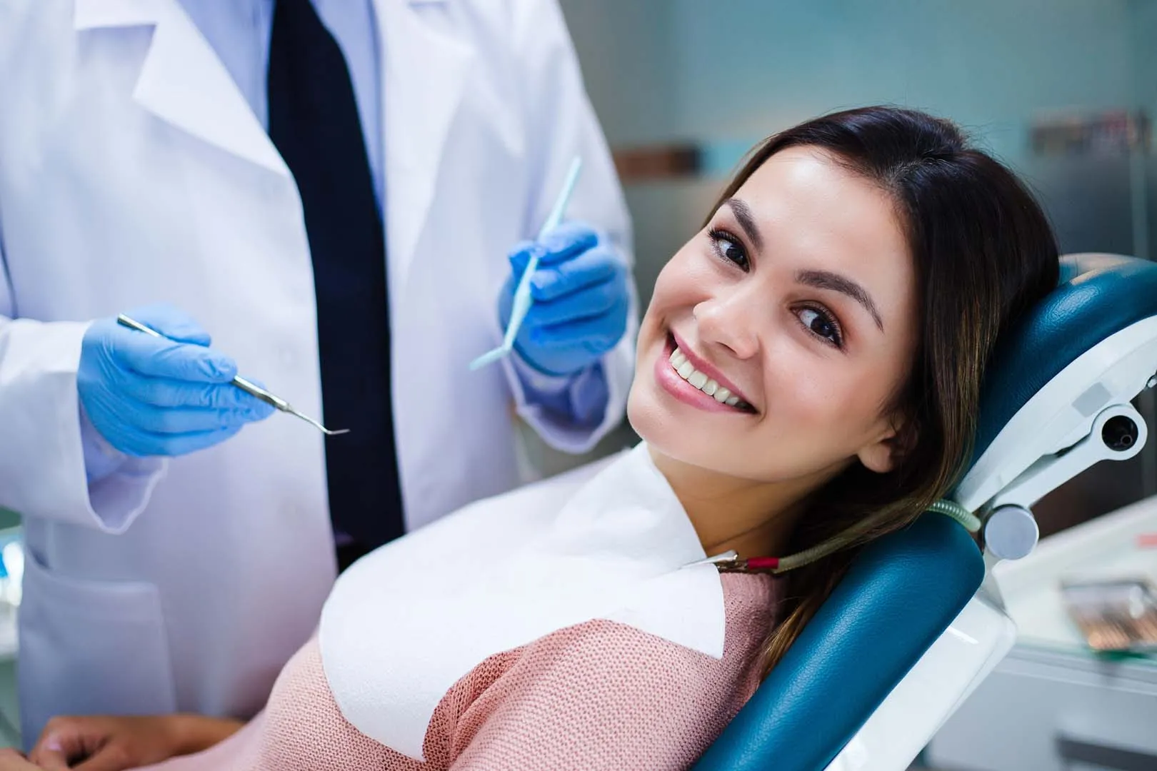 Smiling woman reclining in dental chair with dentist holding dental tools nearby.