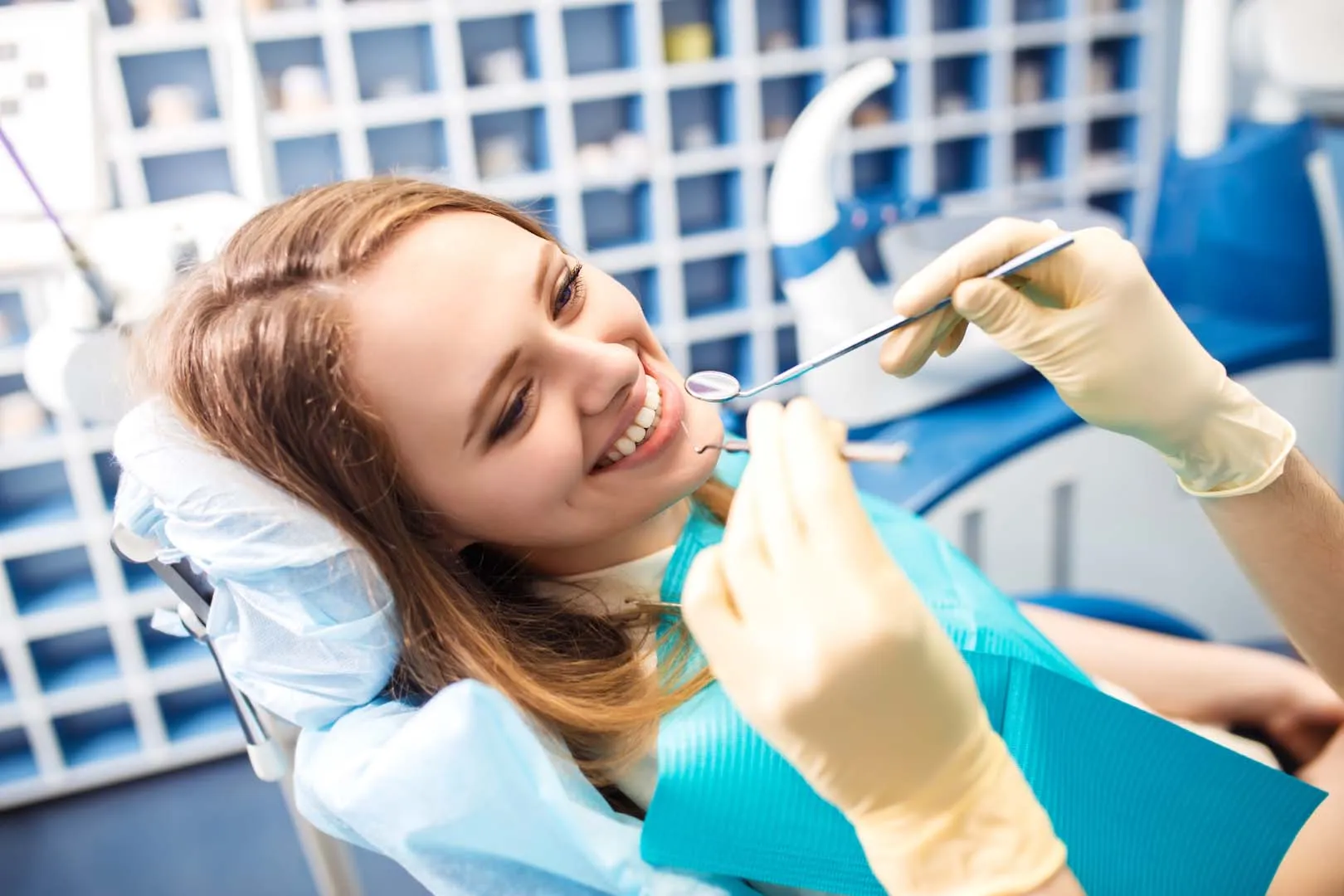 Woman smiling in dental chair as dentist with gloves examines her teeth with dental tools.