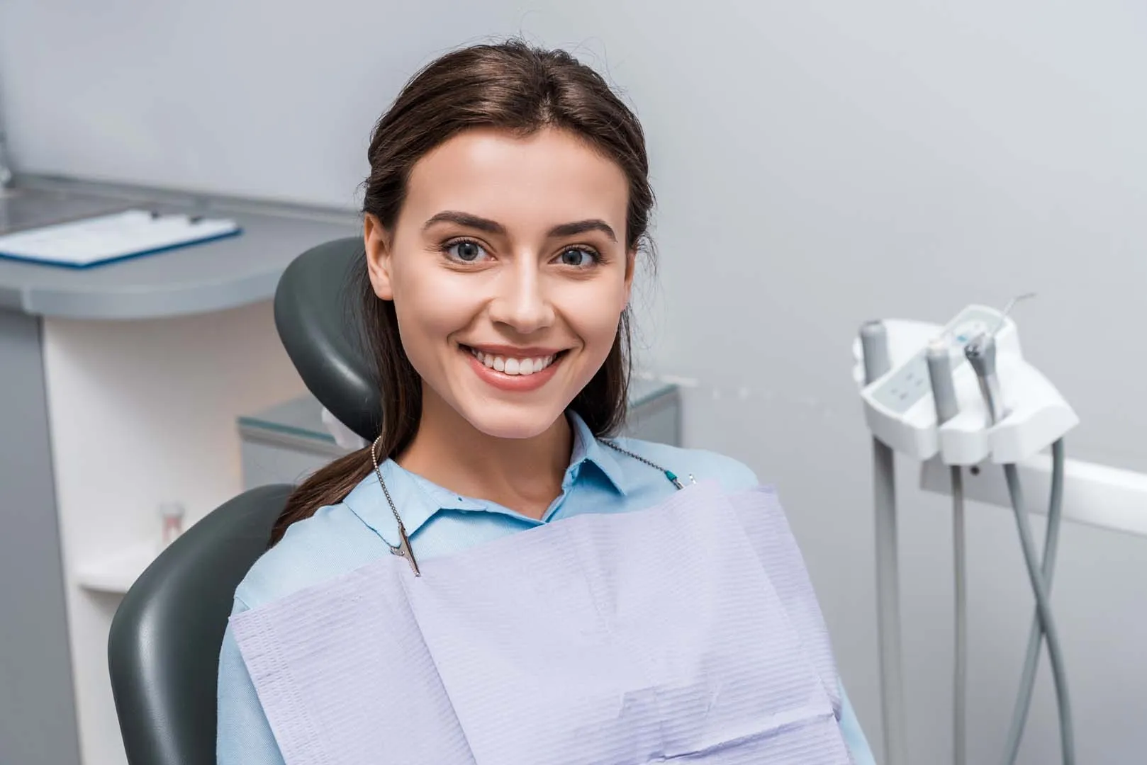 Smiling woman sitting in a dental chair wearing a dental bib in a clinic room.